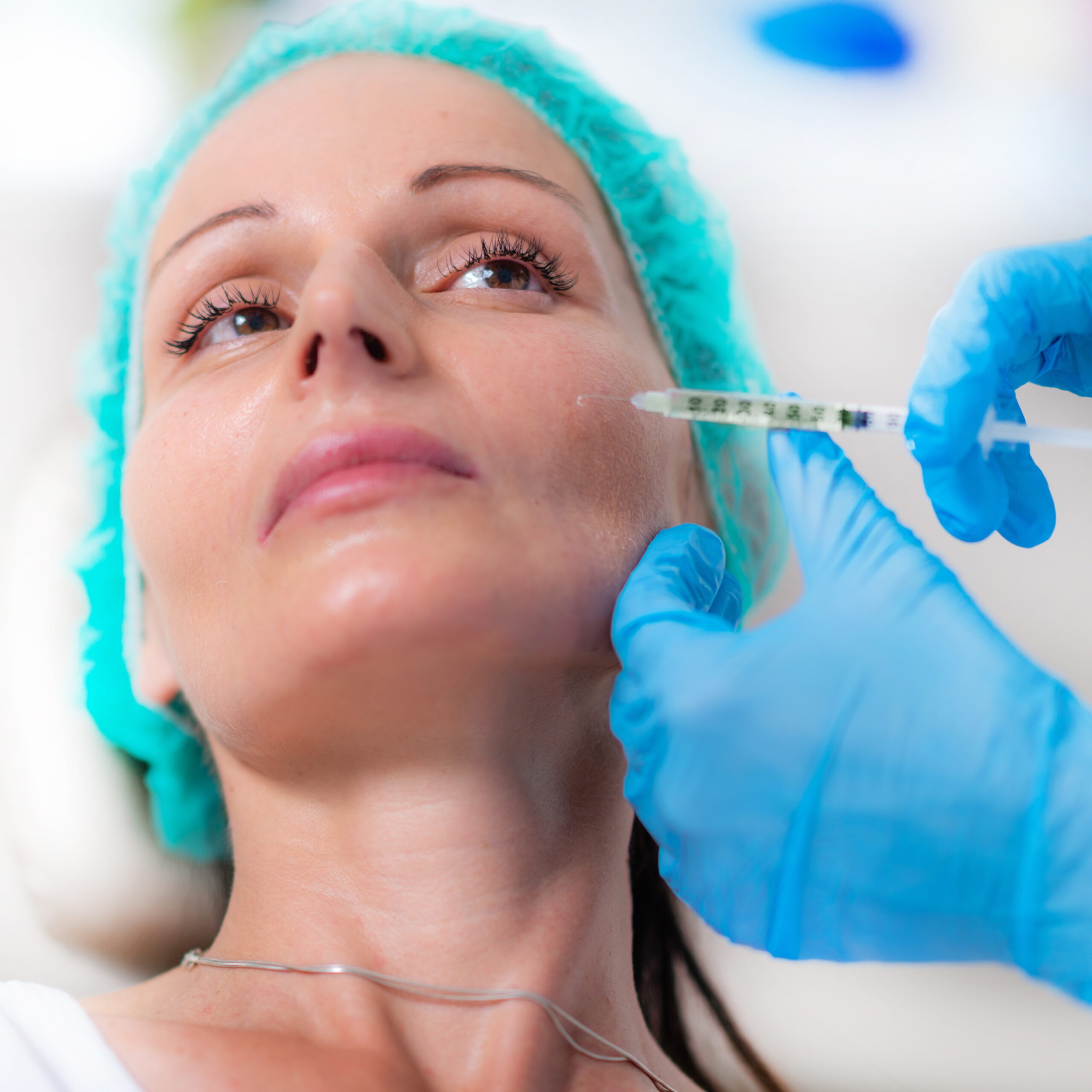 Medical professional administering cheek filler in a sterile clinic environment.