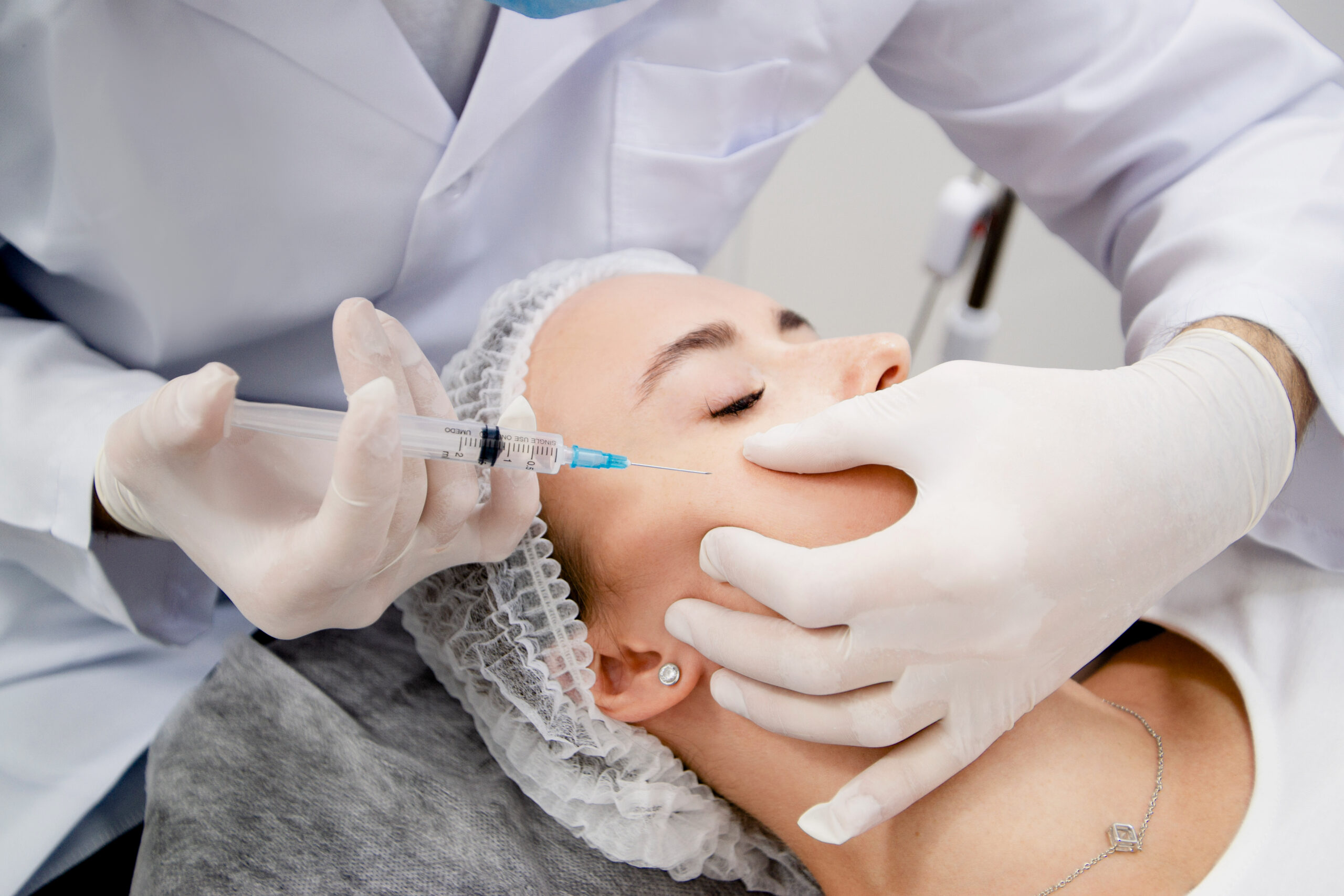 A cosmetologist carefully injecting dermal fillers into a patient’s cheek to enhance facial volume and symmetry.